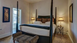 Een hemelbed met een donker hoofdeinde, twee bedlampen en een fauteuil met luipaardprint.