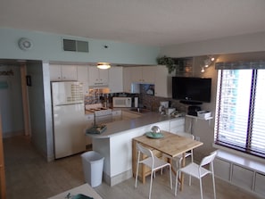 A compact kitchen with white cabinets, a microwave, stove, and a dining area with a wooden table and four chairs.