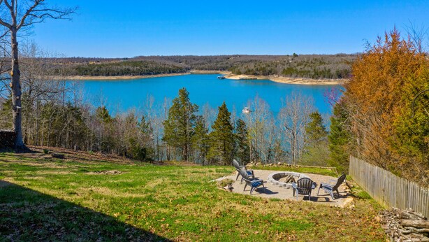 A lakeside view with a clear sky, a wooden deck, and a fire pit area. - The View on Bull Shoals Lake! (Lakeview)