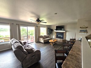A living room with a fireplace, a sofa, a dining area, and a balcony with a view.