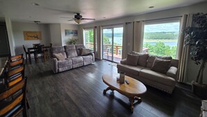 A spacious living room with a large sofa, a coffee table, and a dining area with wooden chairs. - The View on Bull Shoals Lake! (Lakeview)