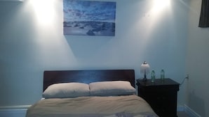 Een slaapkamer met een bed, nachtkastje, lamp en schilderij aan de muur.