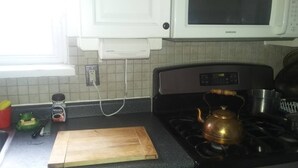 Een keuken met een gasfornuis, een magnetron en een houten snijplank op het aanrecht.