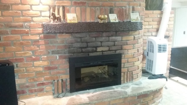 Een bakstenen open haard met een houten plint waarop verschillende objecten staan.