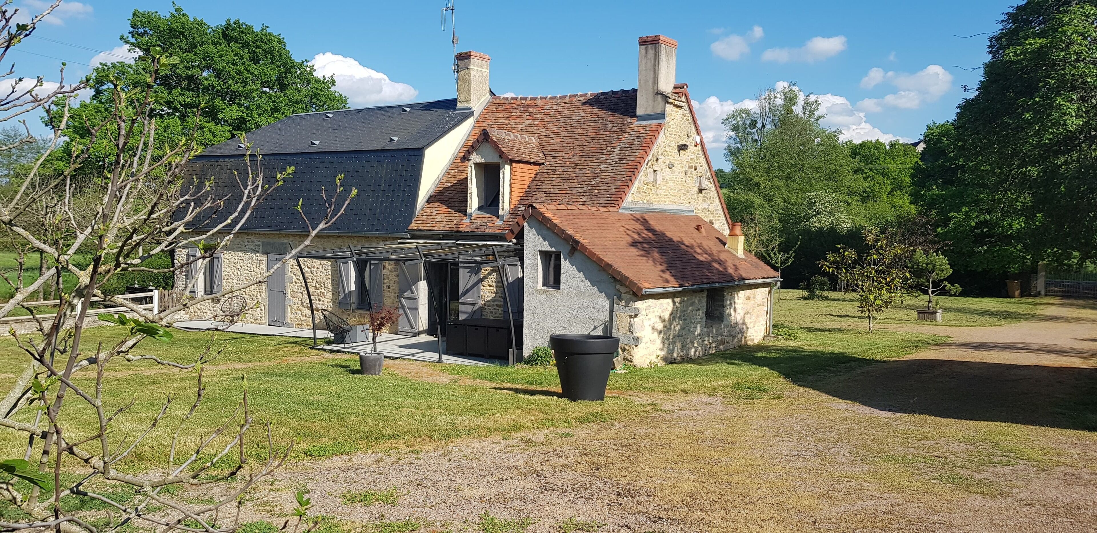 A stone house with a tiled roof, a chimney, and a small attached structure.