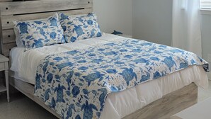 Ein Schlafzimmer mit hölzernem Kopfteil, einem Bett mit blau-weißer maritime Bettdecke, einem Deckenventilator und einer an der Wand befestigten Schildkröten-Dekoration.