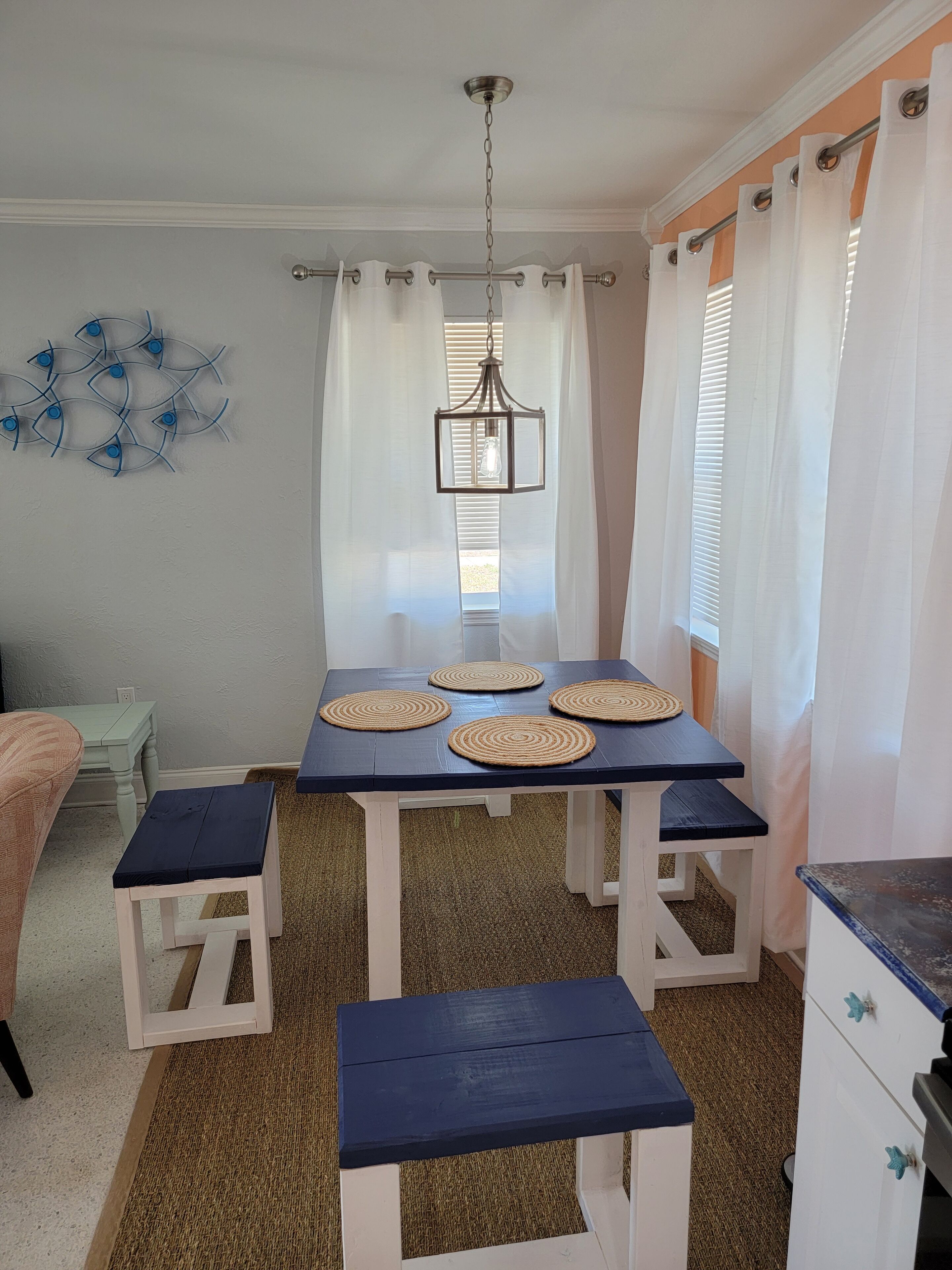 Een eetgedeelte met een tafel voor vier personen, met geweven placemats en een hangende lamp.