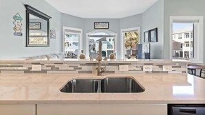 A kitchen with a large island, pendant lights, a built-in sink, and a view of the neighborhood.