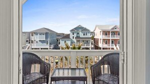 A balcony with wicker chairs and a table, overlooking a row of houses with varying architectural styles.