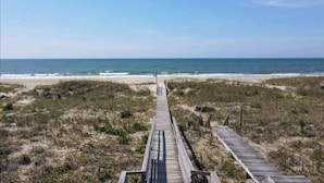 A wooden boardwalk leading to a beach with dunes and sparse vegetation.
