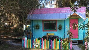 A small, colorful house with a pink door and a blue roof, surrounded by a picket fence.