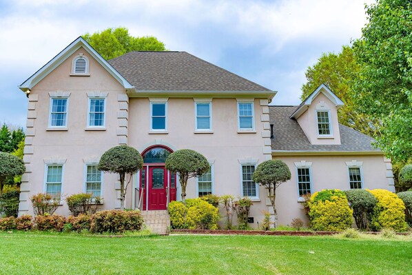 A two-story house with a red door, multiple windows, and a well-maintained lawn.