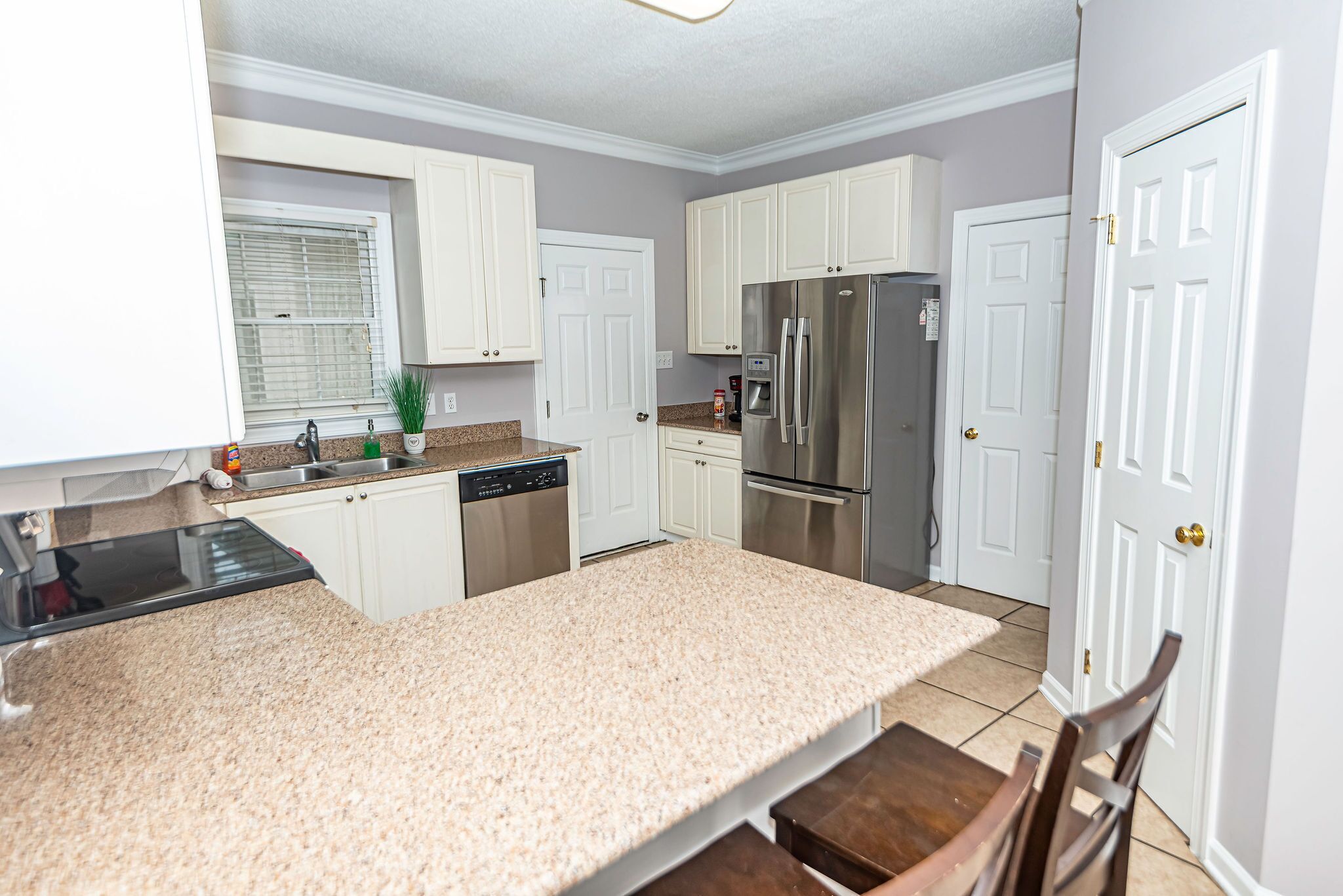 A kitchen with white cabinets, a stainless steel refrigerator, a dishwasher, and a granite countertop.