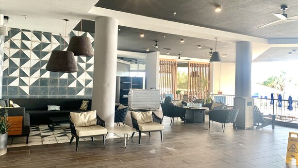 A spacious lobby with a modern design, featuring a geometric patterned wall, a seating area with sofas and chairs, and a large pillar.