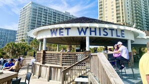 A waterfront restaurant named "Wet Whistle" with outdoor seating and a view of tall buildings in the background.
