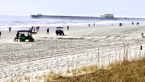 A beach with a pier in the background, sandy terrain, and a golf cart.