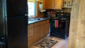 Una cocina con gabinetes de madera, un refrigerador negro, una estufa y un lavamanos.