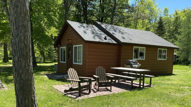 Una cabaña de madera con una mesa de picnic y dos sillas Adirondack en un espacio cubierto de césped.