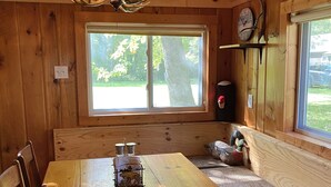 Interior de una cabaña de madera con una mesa de comedor, sillas, un banco y un ventanal grande.