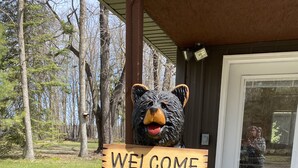 Una escultura de madera de un oso sostiene un letrero que dice "BIENVENIDOS" frente a un edificio con puerta de cristal.
