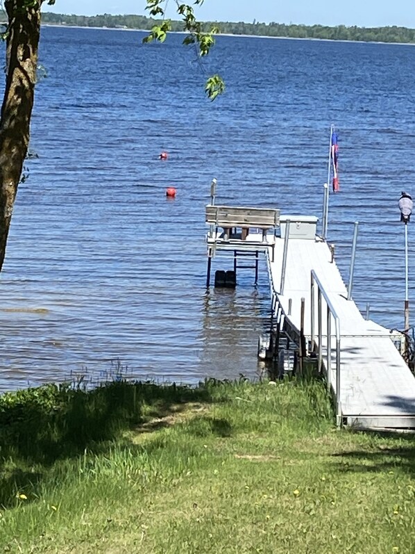 Un muelle se adentra en un lago tranquilo con orilla de hierba y árboles.