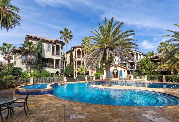 A pool surrounded by palm trees and a building with multiple balconies.