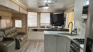 Ein kompaktes Wohnmobil-Interieur mit einer Küchenzeile, einer Sitzecke und einem Deckenventilator.