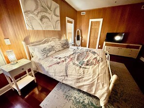 A bedroom with a bed, bedside table, dresser, TV, and a large abstract painting on the wall.