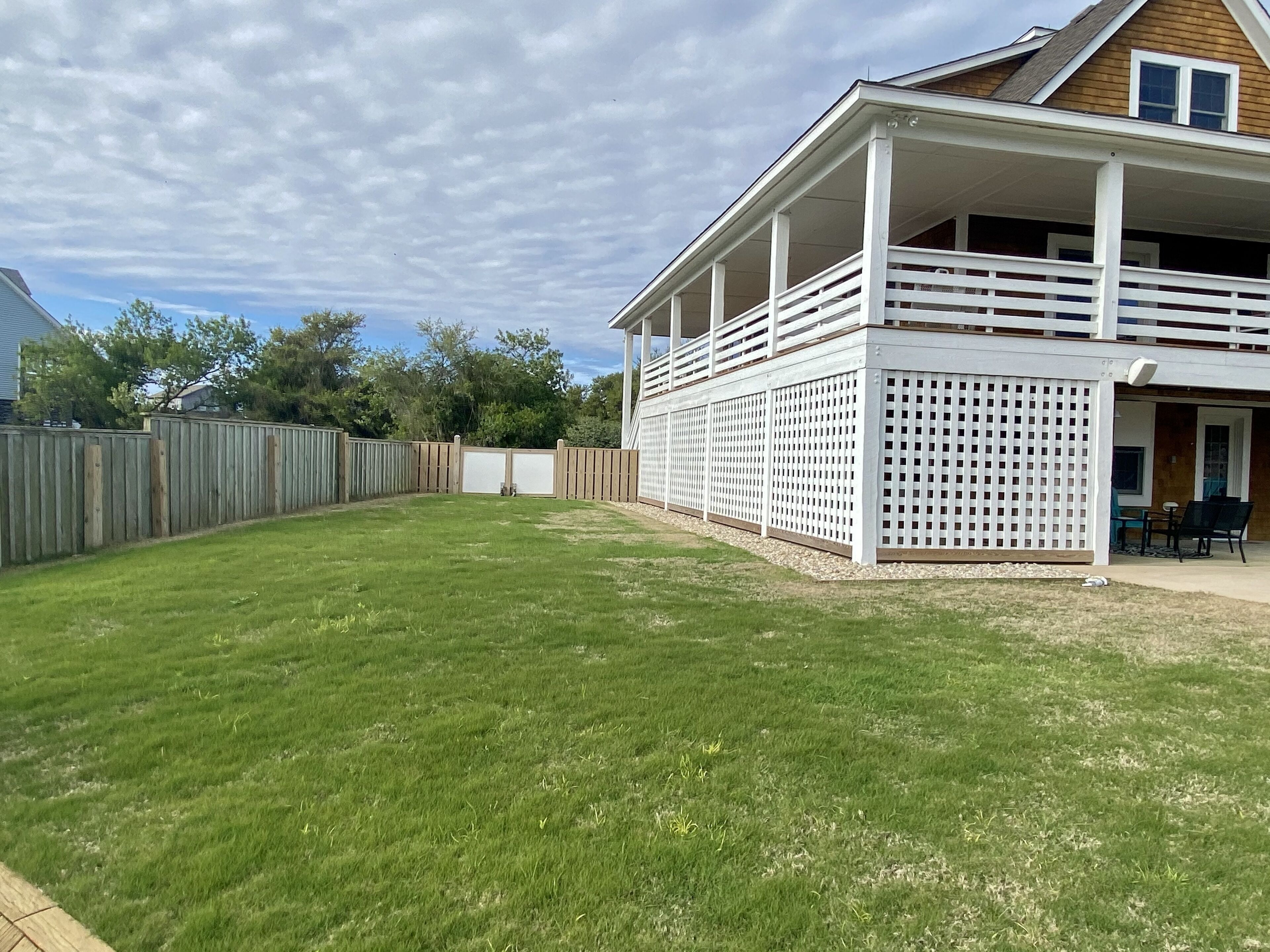 A backyard with a wooden deck, a white fence, and a house with a balcony.
