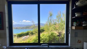 A kitchen with a large window overlooking a scenic landscape, including a body of water and greenery. - Stunning ocean views, Sunsets and just 30 seconds from the Beach! (GA)