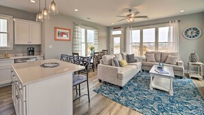 A modern kitchen with white cabinets, a dining area with a table and chairs, a living room with a sofa and coffee table, and large windows with curtains. - 'The Tipsy Flamingo' ~ Incredible Salt Marsh Views (Atlantic Beach)