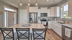 A modern kitchen with white cabinets, stainless steel appliances, and a large island with chairs. - 'The Tipsy Flamingo' ~ Incredible Salt Marsh Views (Atlantic Beach)