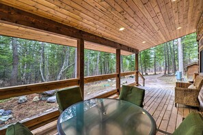 Enjoy a serene forest view from this outdoor deck with a glass-top table and comfortable seating.
