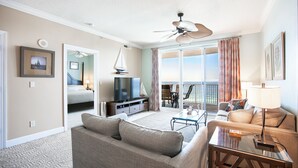 Habitación de hotel con balcón, sofá, televisor, mesa de comedor y ventilador de techo.