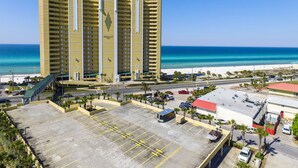 Un hotel de varios pisos con vista a la playa, estacionamiento y un edificio de techo rojo cerca.