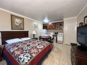 Cozy retreat with a neatly made bed, compact kitchenette, and a functional desk area.