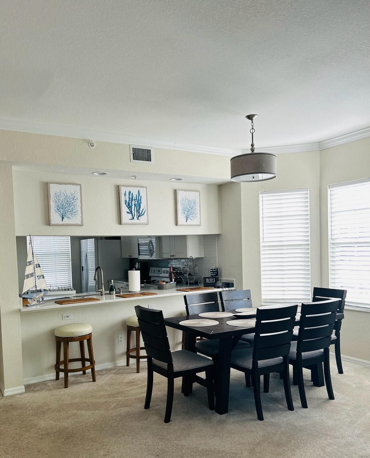 A modern kitchen with a dining area, featuring a central island, bar stools, and a chandelier.