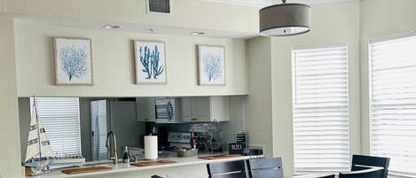 A modern kitchen with a dining area, featuring a central island, bar stools, and a chandelier.