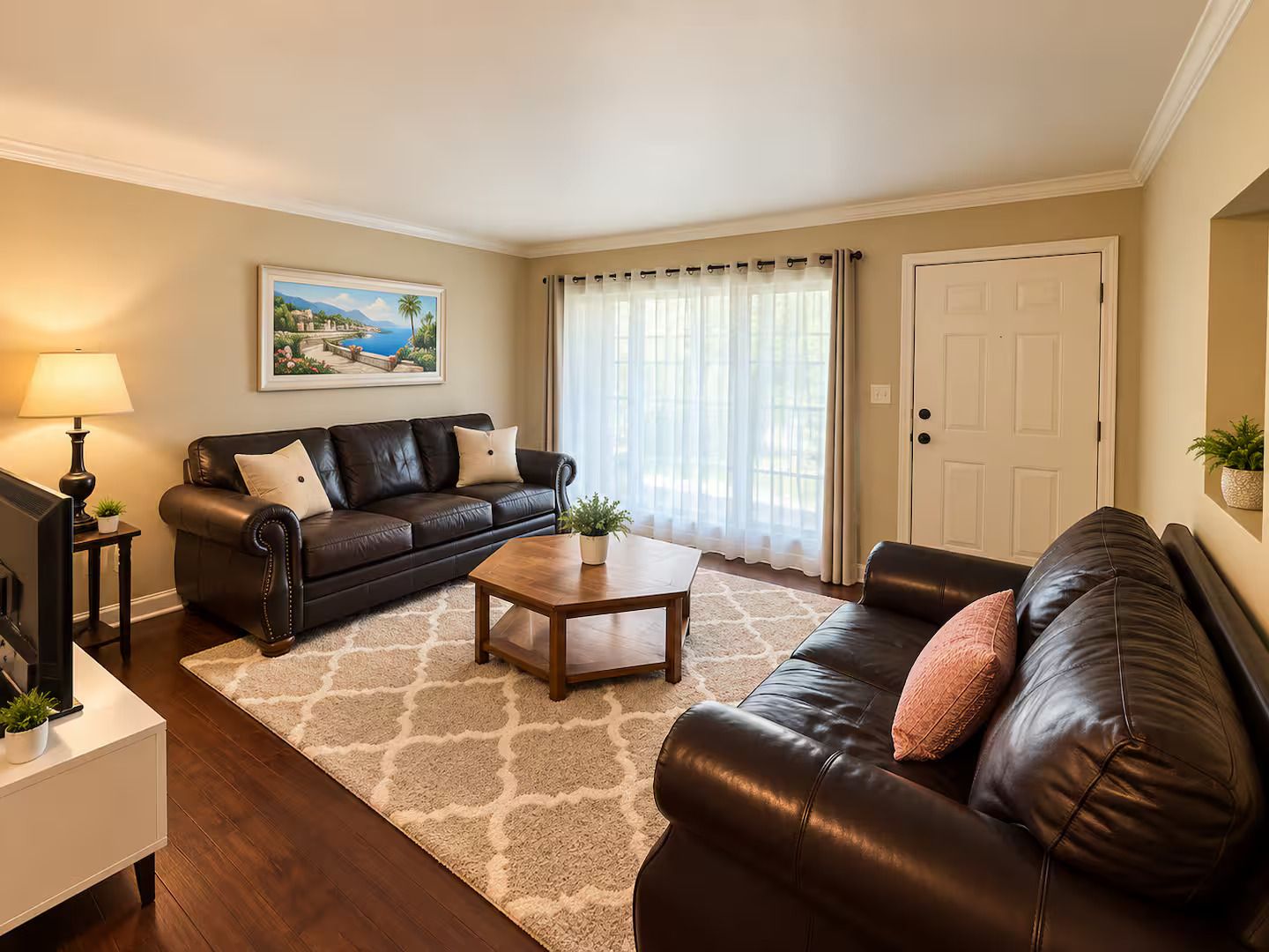 A living room with a dark leather sofa, a wooden coffee table, a TV on a stand, and a painting on the wall.