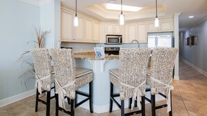 A kitchen with a central island, two bar stools, a microwave, a stove, and pendant lights.
