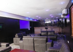 Un área de bar con asientos de cuero, un televisor montado en la pared e iluminación empotrada en el techo.