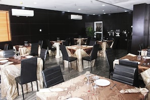 A dining area with tables set for multiple guests, featuring black chairs and tables covered with patterned tablecloths. - Room-royalrex Hotel-guest Room (Lagos)