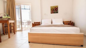 Un dormitorio amplio con una cama grande, una mesita de noche de madera, un escritorio con silla y un balcón con vistas.