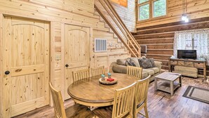 L’intérieur d’un chalet en bois comprend une table à manger, des chaises, un canapé, un téléviseur et un escalier.
