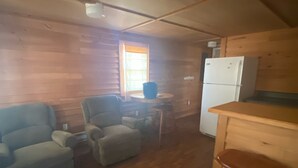Une pièce compacte aux murs lambrissés, comprenant un coin cuisine, un espace repas avec deux chaises et un canapé.