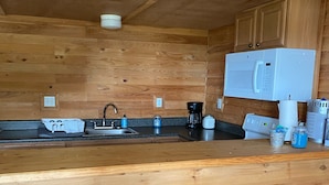 Une cuisine avec des murs en bois, un micro-ondes blanc, une machine à café et deux tabourets.