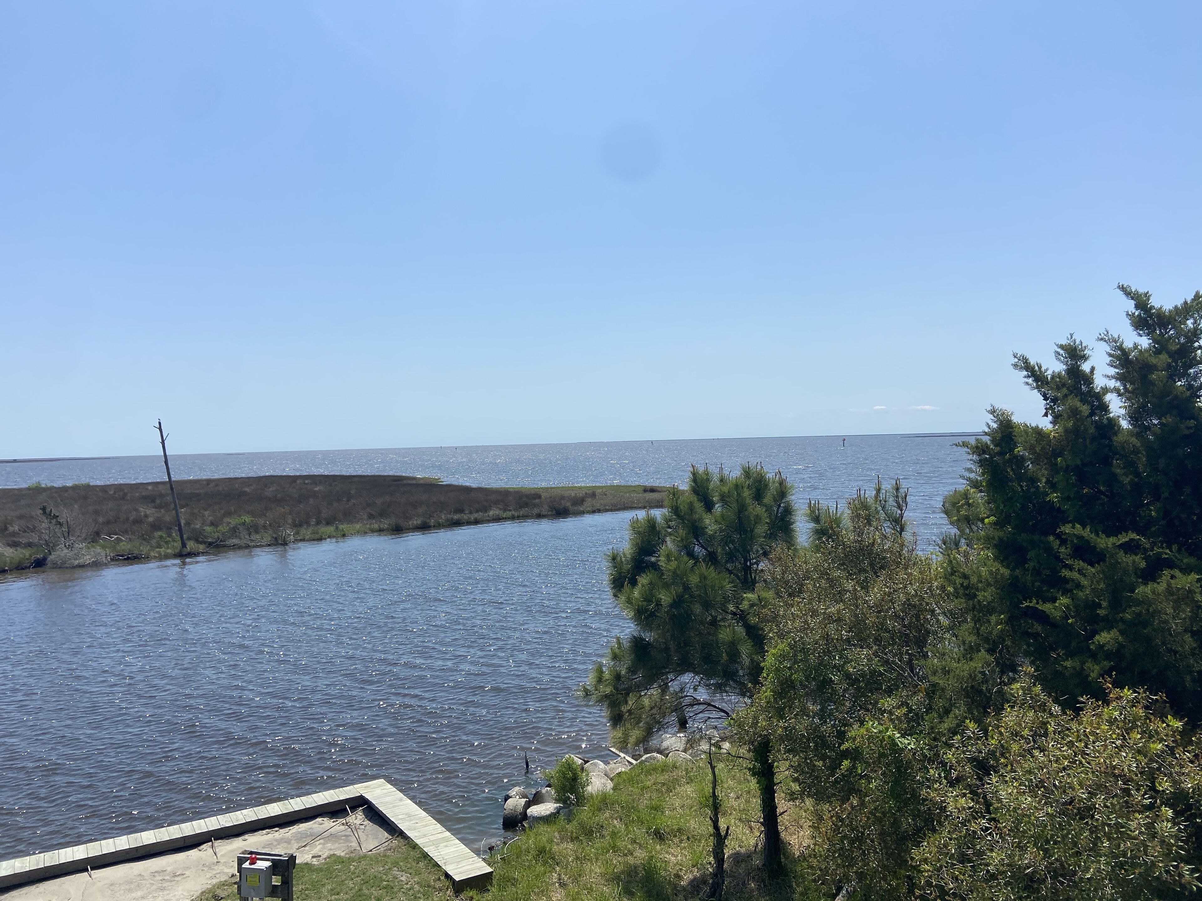 A riverside view with a wooden dock, trees, and a clear sky.