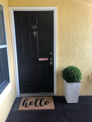 A black door with a 'NO SMOKING' sign, a mailbox, and a 'hello' mat.