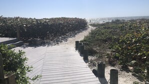 Een houten looppad dat naar een strand leidt, omgeven door dichte begroeiing.