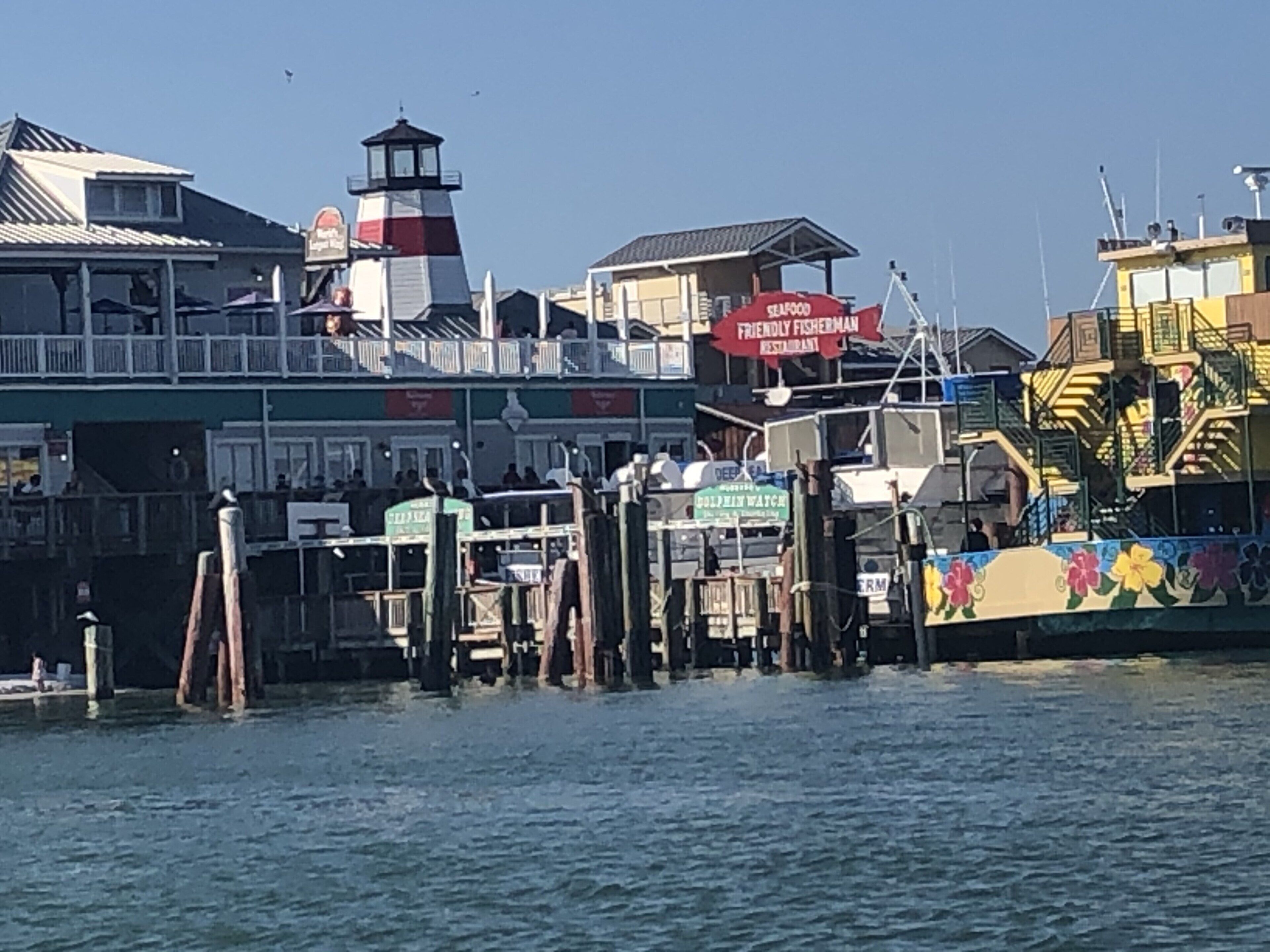A waterfront area with a lighthouse, a restaurant named 'Friendly Fisherman Restaurant', and a colorful mural on a building.